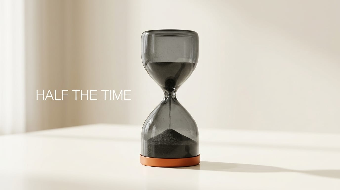 Charcoal hourglass on ivory desk with orange base showing half-empty top bulb: half the workflow time